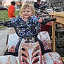 Everlee is registered to the contest to win money with this photo: adult, atv, child, dirt_road, floral_jacket, grass, handlebars, no_helmet, outdoor, people, portrait, quad_bike, smile, sunset, toddler, trailer, trees, truck, vehicle, wooden_table