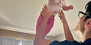 Gabriella is registered to the contest to win money with this photo: baby, child, adult, indoor, curtains, window, smile, glasses, person, joy, hair, lifting, playful, pink_clothing, white_shirt, room, furniture, light, hands, happy