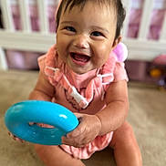 Gabriella joined the competition — help win amazing prizes! baby, smiling, toy, blue_ring, pink_clothing, headband, indoor, carpet, sitting, happy, child, infant, cute, playful, face, hand, foot, cradle, blurred_background, young_child