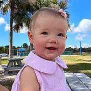 Ayla is registered to the contest to win money with this photo: baby, child, smiling, pink_dress, bow, earrings, outdoor, picnic_table, palm_tree, blue_sky, clouds, grass, park, sunny, happy, person, cute, summer, nature, daytime