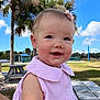 baby, child, smiling, pink_dress, bow, earrings, outdoor, picnic_table, palm_tree, blue_sky, clouds, grass, park, sunny, happy, person, cute, summer, nature, daytime
