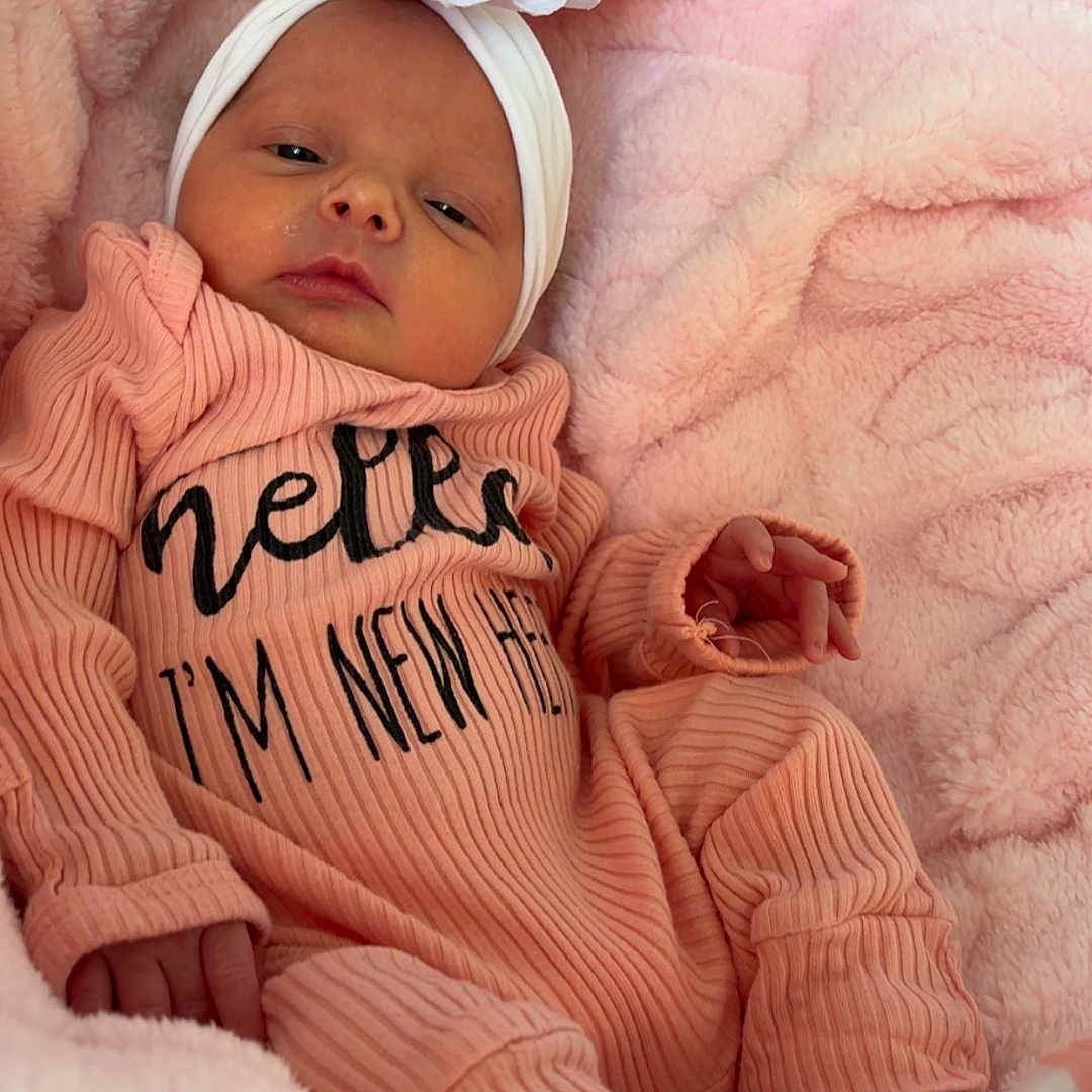 Mckenna is registered to the contest to win money with this photo: newborn, baby, infant, headband, flower, pink_blanket, cozy, sleepy, cute, portrait, clothing, soft_texture, small_hands, baby_sock, lying_down, indoor, closeup, child, person, resting