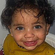 Sofia participe au concours pour gagner de l'argent avec cette photo : toddler, child, curly_hair, blue_eyes, smiling, messy_face, food_stains, yellow_bib, highchair, indoor, portrait, happy, cute, clothing, person, young_child, baby, mealtime, fun, expression