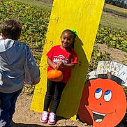 Araelynn Burkett is registered to the contest to win money with this photo: child, girl, pumpkin, pumpkin_patch, height_chart, outdoor, field, sunlight, smile, casual_clothing, sneakers, greenery, nature, daytime, people, playful, autumn, harvest, fun, yard