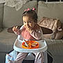 toddler, child, high_chair, food, snack, pink_bow, hair_accessory, bib, pajamas, indoor, living_room, sofa, plate, spoon, cute, baby, person, feeding, seated, smiling