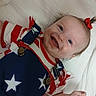baby, child, smiling, happy, red_bow, blue_eyes, white_blanket, stars, stripes, clothing, suspender, infant, portrait, cute, lying_down, small_hand, red_white_blue, patterned_clothing, person, face