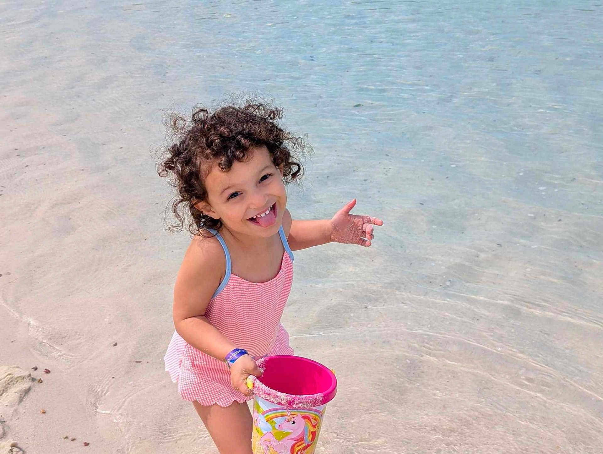 Serena participe au concours pour gagner de l'argent avec cette photo : child, toddler, beach, water, sand, swimsuit, bucket, unicorn, curly_hair, play, happy, smiling, summer, outdoor, fun, toy, shallow_water, cute, vacation, sunny