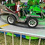 Noah is registered to the contest to win money with this photo: child, toddler, adult, carnival, fair, ride, amusement_ride, car_ride, metal, wheel, seat, safety_belt, green_lights, outdoor, grass, railing, smile, family, people, booth