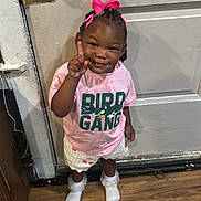 Milan is registered to the contest to win money with this photo: toddler, child, girl, indoor, wooden_floor, pink_bow, hair_accessory, tshirt, shorts, socks, smiling, pointing, door, doorknob, floor, clothing, person, cute, standing, happy
