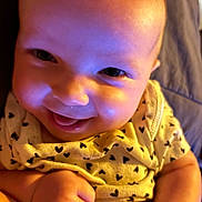 Bailee Rockholt is registered to the contest to win money with this photo: baby, infant, smiling, close_up, onesie, hearts_pattern, eyes, cheeks, hand, fist, skin, head, portrait, adorable, happy, candid, colorful_lighting, purple_tint, blanket, lying_down