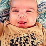 baby, infant, smiling, face, portrait, blanket, patterned_blanket, eyes, mouth, cheeks, tshirt, logo, nike_logo, animal_print, leopard_print, skin, closeup, happy, indoors, cute