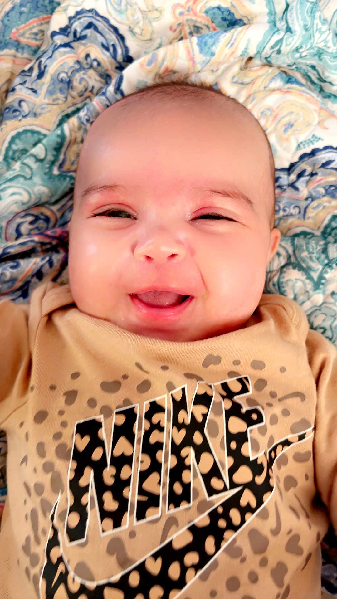 Azula is registered to the contest to win money with this photo: baby, infant, smiling, face, portrait, blanket, patterned_blanket, eyes, mouth, cheeks, tshirt, logo, nike_logo, animal_print, leopard_print, skin, closeup, happy, indoors, cute