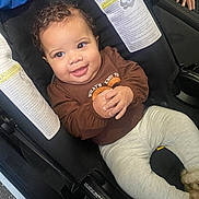 Cataleya is registered to the contest to win money with this photo: baby, child, car_seat, smiling, curly_hair, brown_shirt, gray_pants, happy, cute, infant, hands_clasped, indoor, seatbelt, safety, portrait, person, clothing, footwear, cozy, adorable