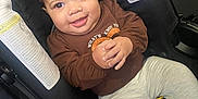 Cataleya is registered to the contest to win money with this photo: baby, child, car_seat, smiling, curly_hair, brown_shirt, gray_pants, happy, cute, infant, hands_clasped, indoor, seatbelt, safety, portrait, person, clothing, footwear, cozy, adorable