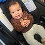 baby, child, car_seat, smiling, curly_hair, brown_shirt, gray_pants, happy, cute, infant, hands_clasped, indoor, seatbelt, safety, portrait, person, clothing, footwear, cozy, adorable