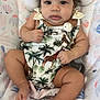baby, infant, child, curly_hair, tropical_outfit, giraffe_print, palm_trees, pacifier_clip, cushioned_seat, floral_pattern, pastel_colors, chubby_cheeks, barefoot, cute, indoors, portrait, relaxed, looking_at_camera, skin, baby_clothing