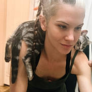 Dove is registered to the contest to win money with this photo: arm, braided_hair, casual, cat, companion, face, friendly, hair, indoor, mirror, pet, reflection, relaxed, shoulder, skin, smile, tabby_cat, tank_top, tattoo, woman