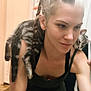 arm, braided_hair, casual, cat, companion, face, friendly, hair, indoor, mirror, pet, reflection, relaxed, shoulder, skin, smile, tabby_cat, tank_top, tattoo, woman