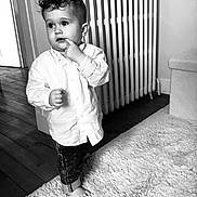 Bixente participe au concours pour gagner de l'argent avec cette photo : toddler, child, indoor, barefoot, white_shirt, curly_hair, carpet, radiator, wooden_floor, curious, standing, monochrome, black_and_white, rolled_jeans, portrait, person, home, expression, cozy, floor