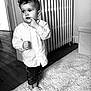 toddler, child, indoor, barefoot, white_shirt, curly_hair, carpet, radiator, wooden_floor, curious, standing, monochrome, black_and_white, rolled_jeans, portrait, person, home, expression, cozy, floor