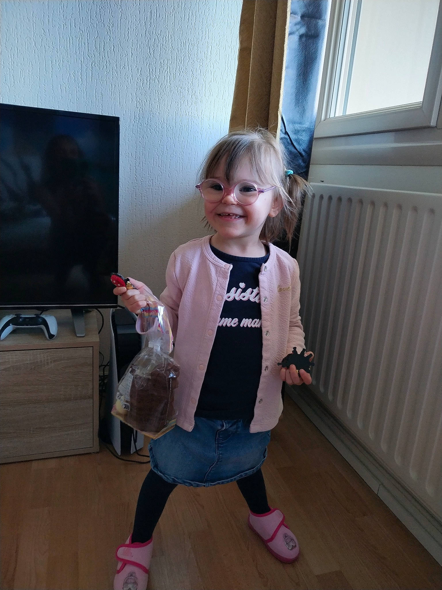 Elilya participe au concours pour gagner de l'argent avec cette photo : baby_toddler_clothing, curtain, eyewear, flooring, fun, hardwood, human_leg, joy, knee, led_backlit_lcd_display, person, room, sandal, sleeve, smile, sock, standing, television, television_set, toddler