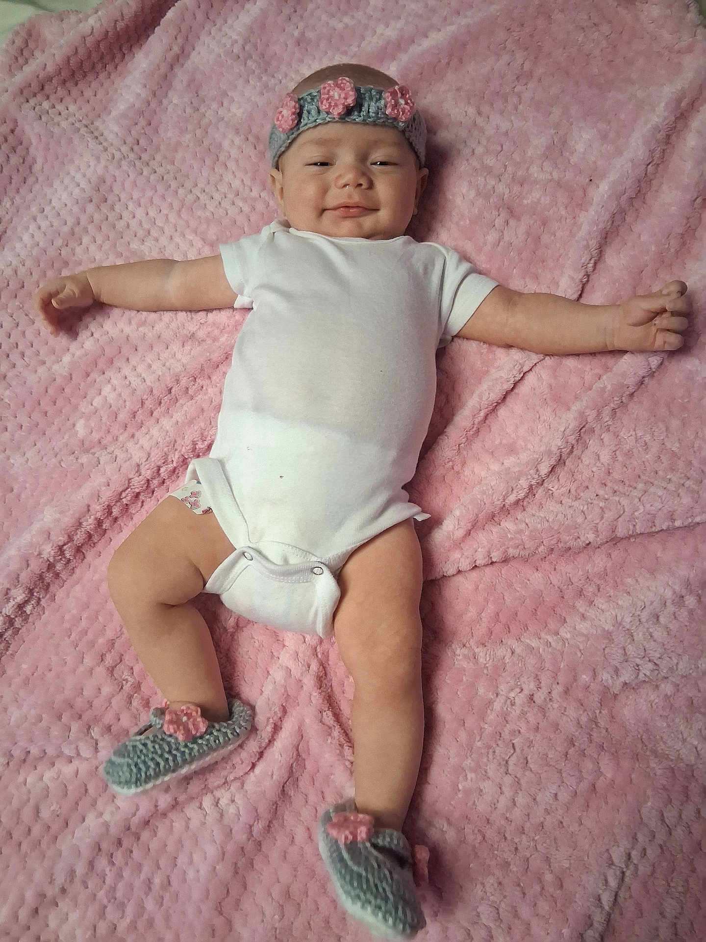 D'Nola is registered to the contest to win money with this photo: baby, blanket, child, cozy, crocheted, cute, footwear, happy, headband, indoors, infant, lying_down, onesie, person, pink, portrait, relaxed, skin, smiling, soft_texture