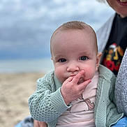 Céleste a rejoint le concours — aidez-le/la à gagner de superbes lots ! baby, child, infant, face, hand, knitted_cardigan, unicorn_shirt, adult, smile, cozy, grey_sweater, outdoor, beach, cloudy_sky, closeup, portrait, cute, curious, holding, fingers