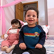 Kenan joined the competition — help win amazing prizes! toddler, child, doll, bed, pink_canopy, blue_sweater, knitted_overalls, socks, indoor, smiling, happy, portrait, person, furniture, door, room, hair, face, toy, seated