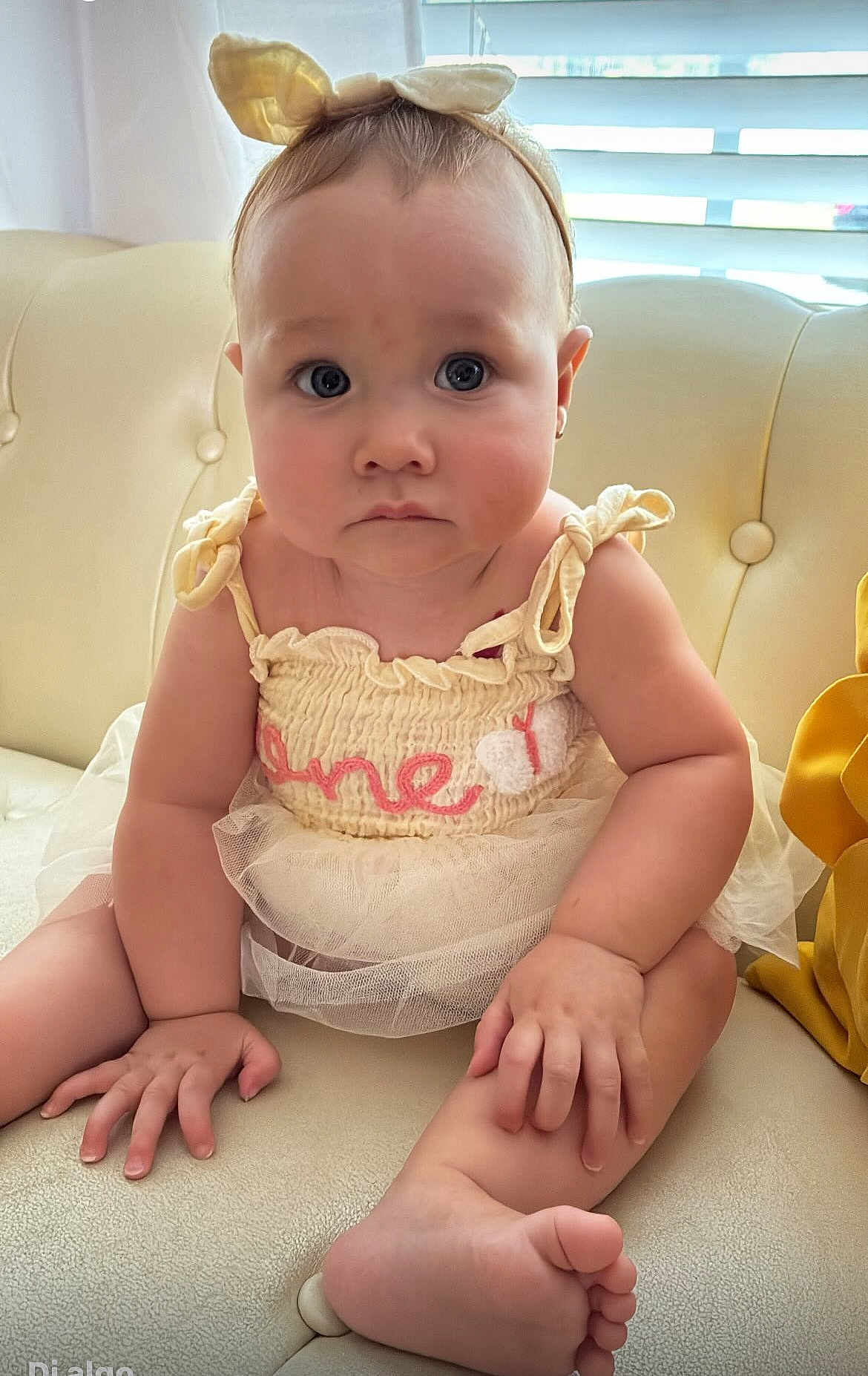 Leah joined the competition — help win amazing prizes! baby, infant, child, headband, bunny_ears, dress, cream_sofa, sitting, curious, face, hands, feet, indoors, window, natural_light, cute, portrait, closeup, childhood, expression