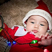 Eduardo joined the competition — help win amazing prizes! baby, christmas, holiday, lights, red_clothing, santa_hat, cute, festive, infant, playing, colorful_lights, fluffy_blanket, indoors, portrait, closeup, child, holiday_season, celebration, soft_texture, adorable