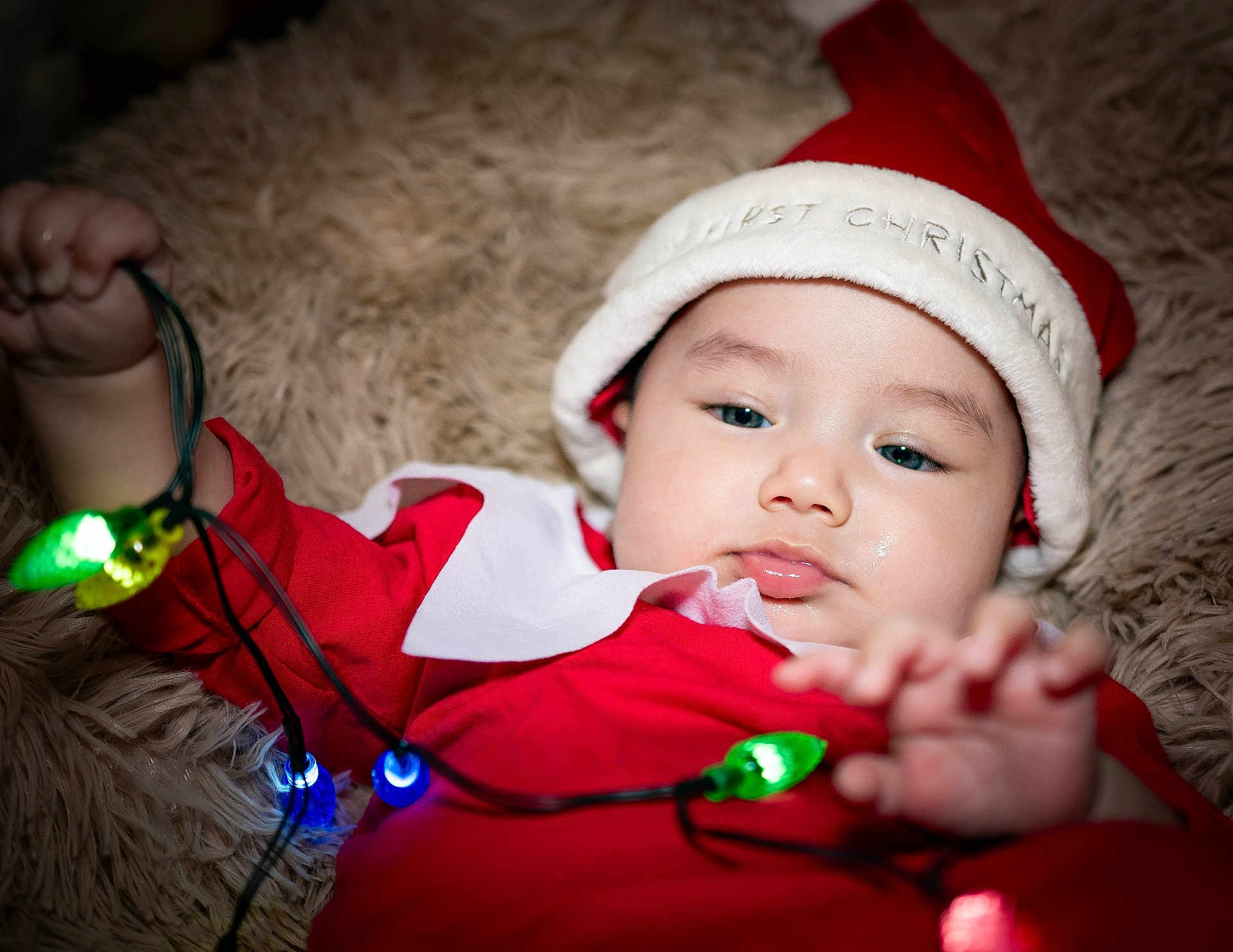 Eduardo joined the competition — help win amazing prizes! baby, christmas, holiday, lights, red_clothing, santa_hat, cute, festive, infant, playing, colorful_lights, fluffy_blanket, indoors, portrait, closeup, child, holiday_season, celebration, soft_texture, adorable