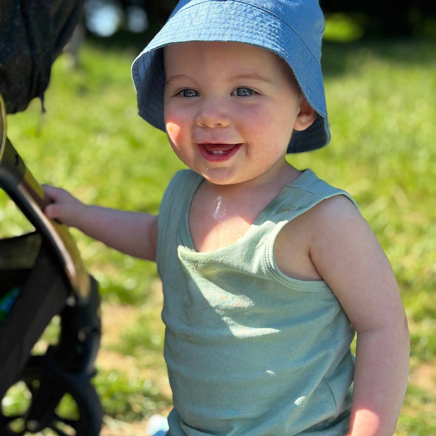 Aaron is registered to the contest to win money with this photo: baby, blue_hat, casual_clothing, child, cute, daylight, grass, happy, nature, outdoor, person, playful, portrait, smiling, stroller, summer, sunlight, tank_top, toddler, young_child