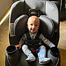 baby, car_seat, child, smiling, seatbelt, indoor, footwear, socks, black, plastic, door, floor, car_seat_cup_holder, head_support, clothing, infant, person, safety, cosco_kids, happy