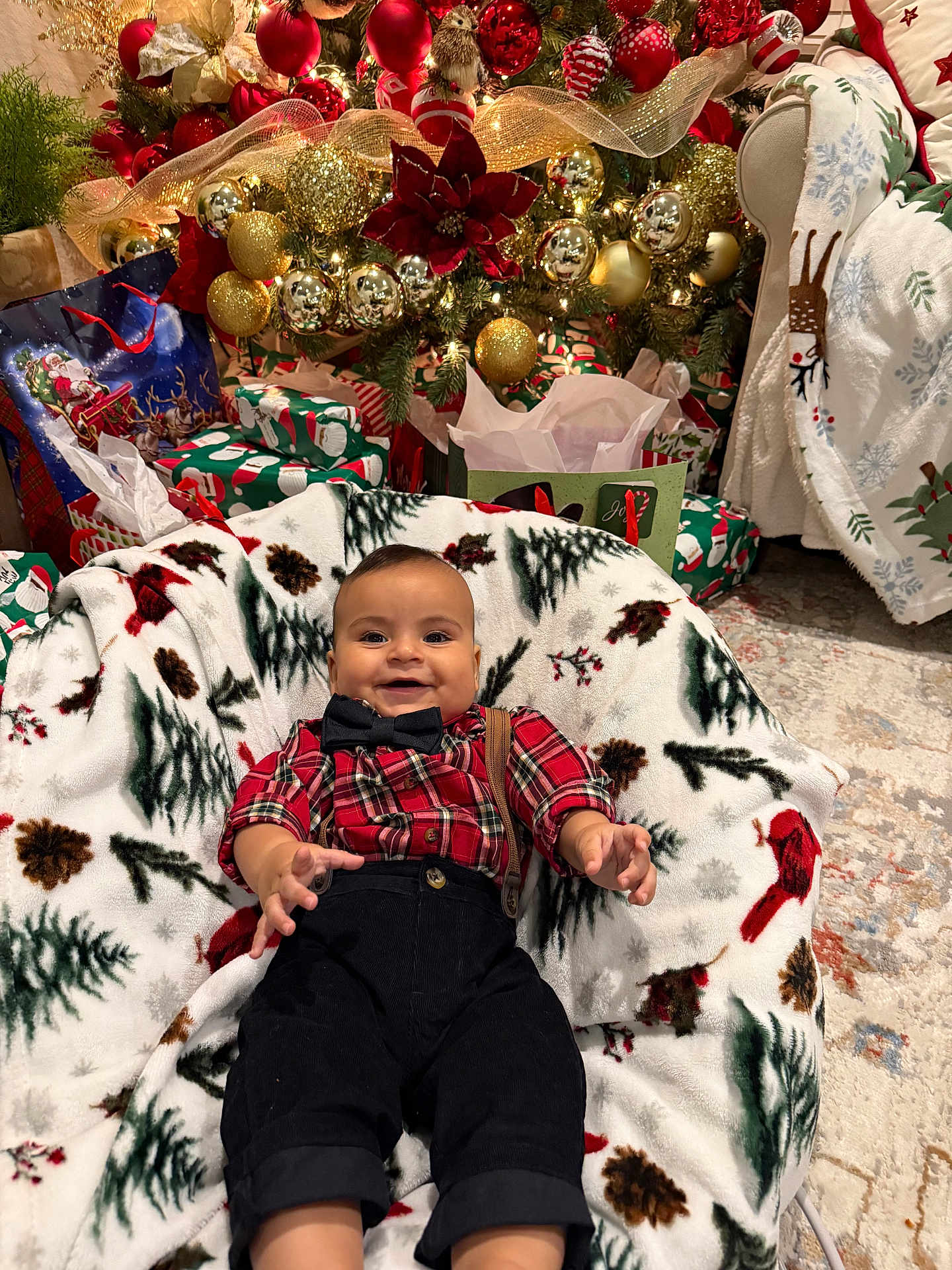 Dylan joined the competition — help win amazing prizes! baby, child, smiling, christmas_tree, christmas_decorations, ornaments, holiday, presents, blanket, plaid_shirt, bow_tie, suspenders, indoors, festive, celebration, carpet, chair, happy, smile, seasonal