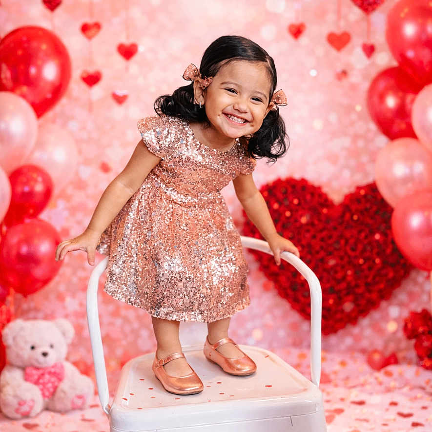 Melani Garcia is registered to the contest to win money with this photo: child, girl, smiling, dress, sparkly, chair, balloons, hearts, pink, red, background, celebration, cute, happy, standing, portrait, hair_bows, indoor, teddy_bear, decorations