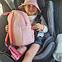 child, car_seat, backpack, pink_hat, smiling, seatbelt, car_interior, window, sunlight, casual_clothing, happy, young_girl, blue_shorts, holding, sitting, seat, safety, travel, person, kid