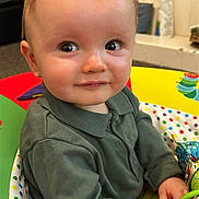 Owen is registered to the contest to win money with this photo: baby, child, clothing, colorful, cute, eyes, face, green_shirt, hands, happy, indoor, infant, looking, person, play_seat, portrait, sitting, smile, toy, young