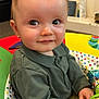 baby, child, clothing, colorful, cute, eyes, face, green_shirt, hands, happy, indoor, infant, looking, person, play_seat, portrait, sitting, smile, toy, young