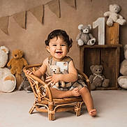 Tomy participe au concours pour gagner de l'argent avec cette photo : toddler, child, smiling, wicker_chair, teddy_bear, plush_toy, brown, cream, curly_hair, cute, happy, sitting, wooden_crate, bunting_flags, indoor, portrait, baby_clothes, floor, decor, cozy