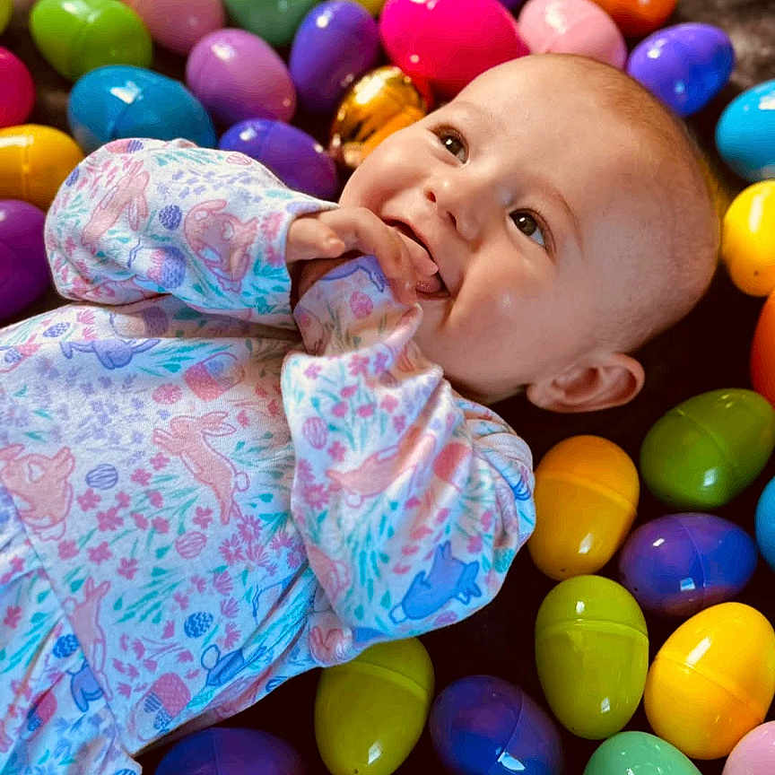 Ryleigh joined the competition — help win amazing prizes! baby, celebration, child, closeup, colorful, cute, easter_eggs, festive, happy, holiday, indoor, infant, lying_down, onesie, patterned_clothing, plastic_eggs, playful, portrait, smile, soft_lighting