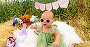 Elena joined the competition — help win amazing prizes! baby, blanket, celebration, child, cute, footwear, fun, grass, green_dress, half_birthday, nature, outdoor, party_hat, pink, plush_toys, portrait, sitting, sunglasses, sunny, wildflowers