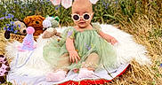 Elena is registered to the contest to win money with this photo: baby, child, sunglasses, green_dress, plush_toys, party_hat, wildflowers, field, grass, blanket, half_birthday, banner, outdoor, cute, sitting, pink_socks, headwear, nature, celebration, portrait