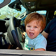 Harvey Ruiz joined the competition — help win amazing prizes! toddler, child, car, steering_wheel, interior, daylight, happy, excited, person, short_sleeves, seat, automobile, young_child, hair, smile, open_mouth, window, dashboard, seatbelt, adult_arm