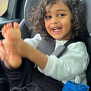 Vedh is registered to the contest to win money with this photo: black_pants, car_interior, car_seat, child, clothing, curly_hair, expression, feet, hair, happy, indoor, person, playful, portrait, seat, seatbelt, smile, water_bottle, white_shirt, window