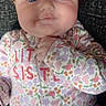baby, infant, child, portrait, face, blue_eyes, wide_eyed, serious_expression, floral_clothing, onesie, baby_clothing, sitting, lying_down, hand, indoor, close_up, colorful, textile, cozy, photography