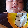 baby, infant, sleeping, face, portrait, blanket, wrapped, cozy, indoors, close_up, peaceful, resting, couch, textile, patterned_blanket, warm_lighting, head, closed_eyes, mouth, cute