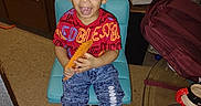 Jonas joined the competition — help win amazing prizes! child, smiling, indoor, chair, comb, red_shirt, blue_jeans, crocs, kitchen, cabinet, sunflower, plant, backpack, glass_table, floor, happy, person, young_child, seated, casual_clothing
