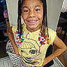 child, girl, smile, braided_hair, beads, yellow_shirt, cartoon_print, patterned_pants, indoor, laundry_basket, tiled_floor, standing, confident, happy, person, home, casual_clothing, earrings, portrait, hands_on_hips