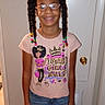 child, girl, smiling, standing, glasses, braided_hair, beads, tshirt, jeans, indoor, door, bracelets, hair_ties, wood_floor, thermostat, casual_clothing, portrait, happy, person, home