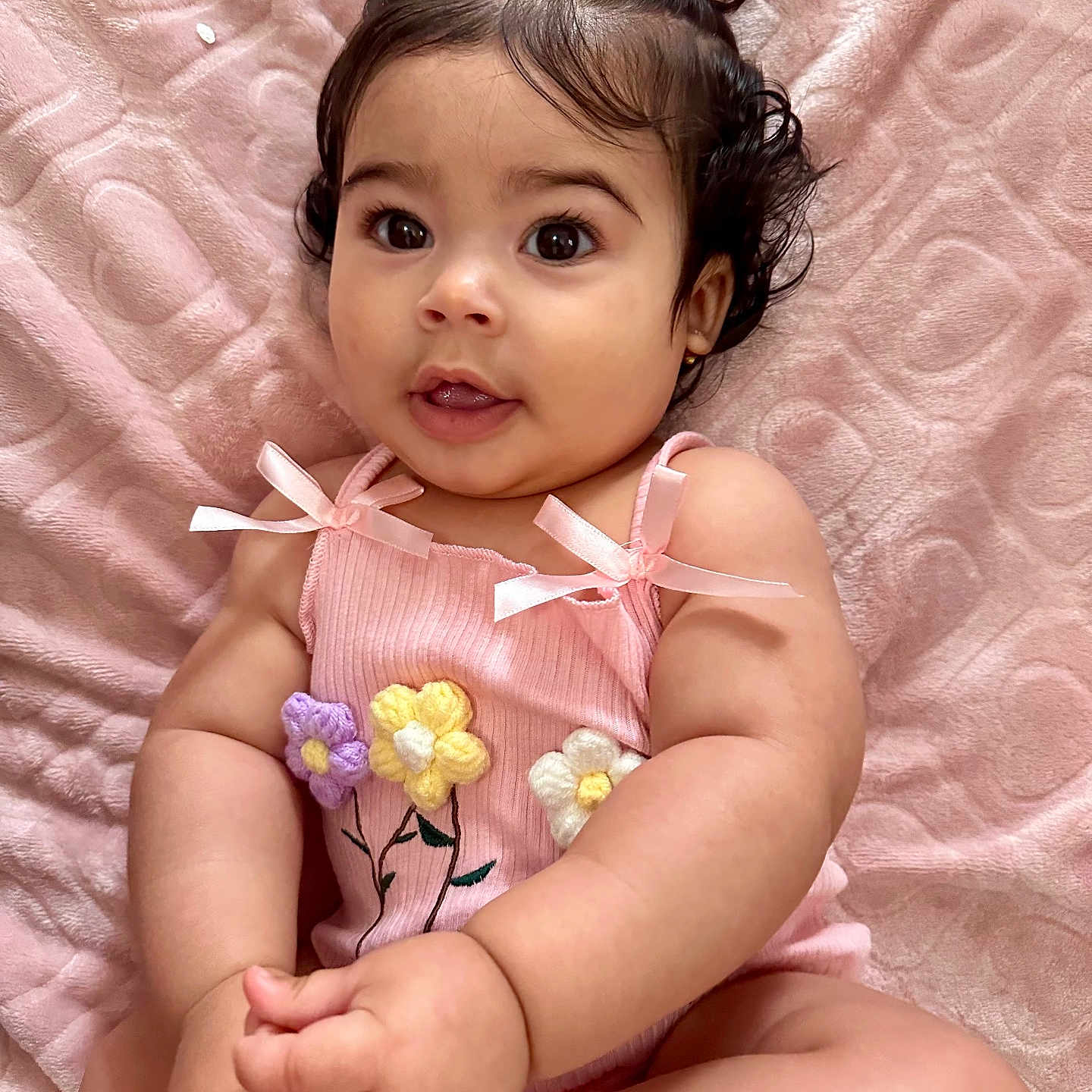 Ailana Martinez is registered to the contest to win money with this photo: baby, blanket, bows, child, clothing, curious, cute, flowers, hands, indoors, infant, knitted, legs, pigtails, pink, portrait, sitting, skin, smiling, soft